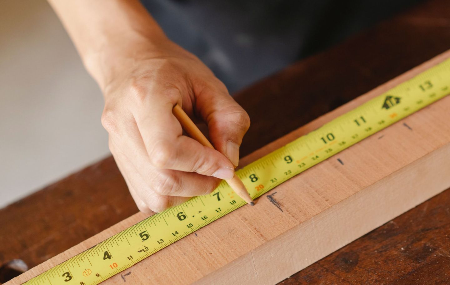 Hände reißen mit Bleistift und Bandmaß ein Maß auf einer gehobelten Bohle an