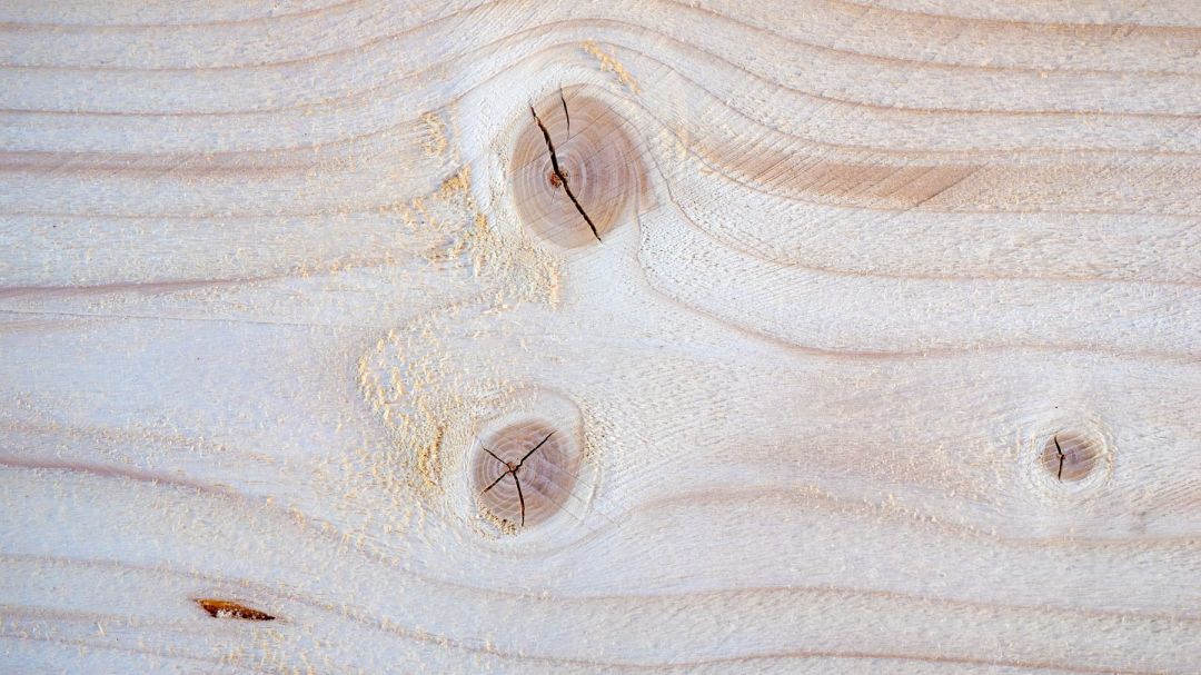 Nahaufnahme einer gehobelten Nadelholzbohle mit drei Ästen und geschwungenem Faserbild